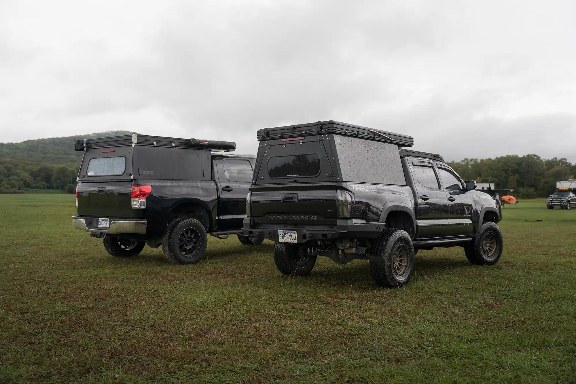 Black Toyota truck with Go Fast Camper next to another black Toyota truck with Madix Drift Truck Bed Camper in a field.
