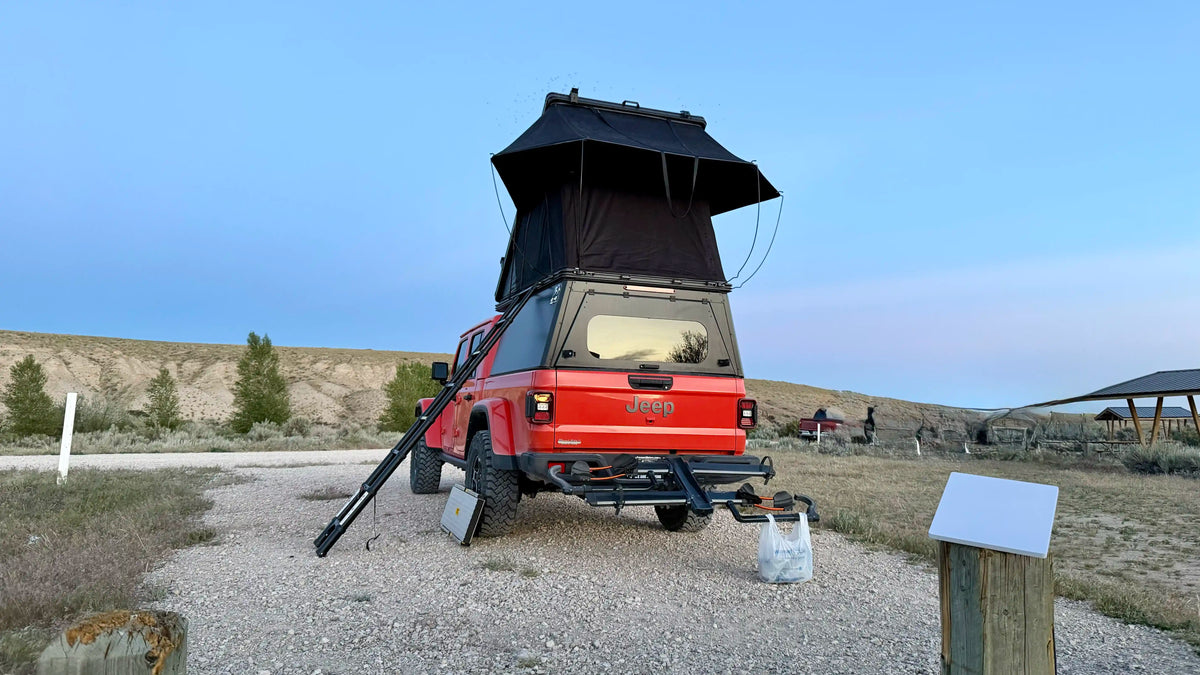 Jeep gladiator with truck bed camper and rooftop tent at a campsite.