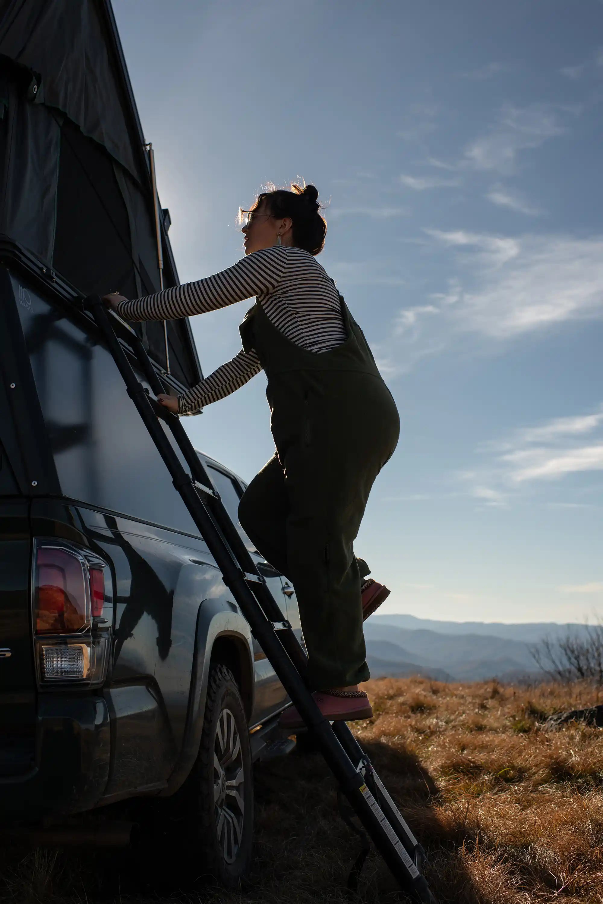 Person climbing ladder to get into rooftop tent on top of truck bed camper