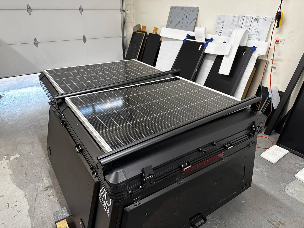 A black truck bed camper woth rooftop tent with two large solar panels mounted on top.