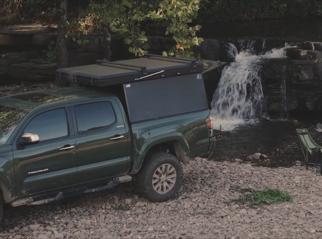 Green Toyota Tacoma next to a waterfall with Madix Outdoors drift truck camper.