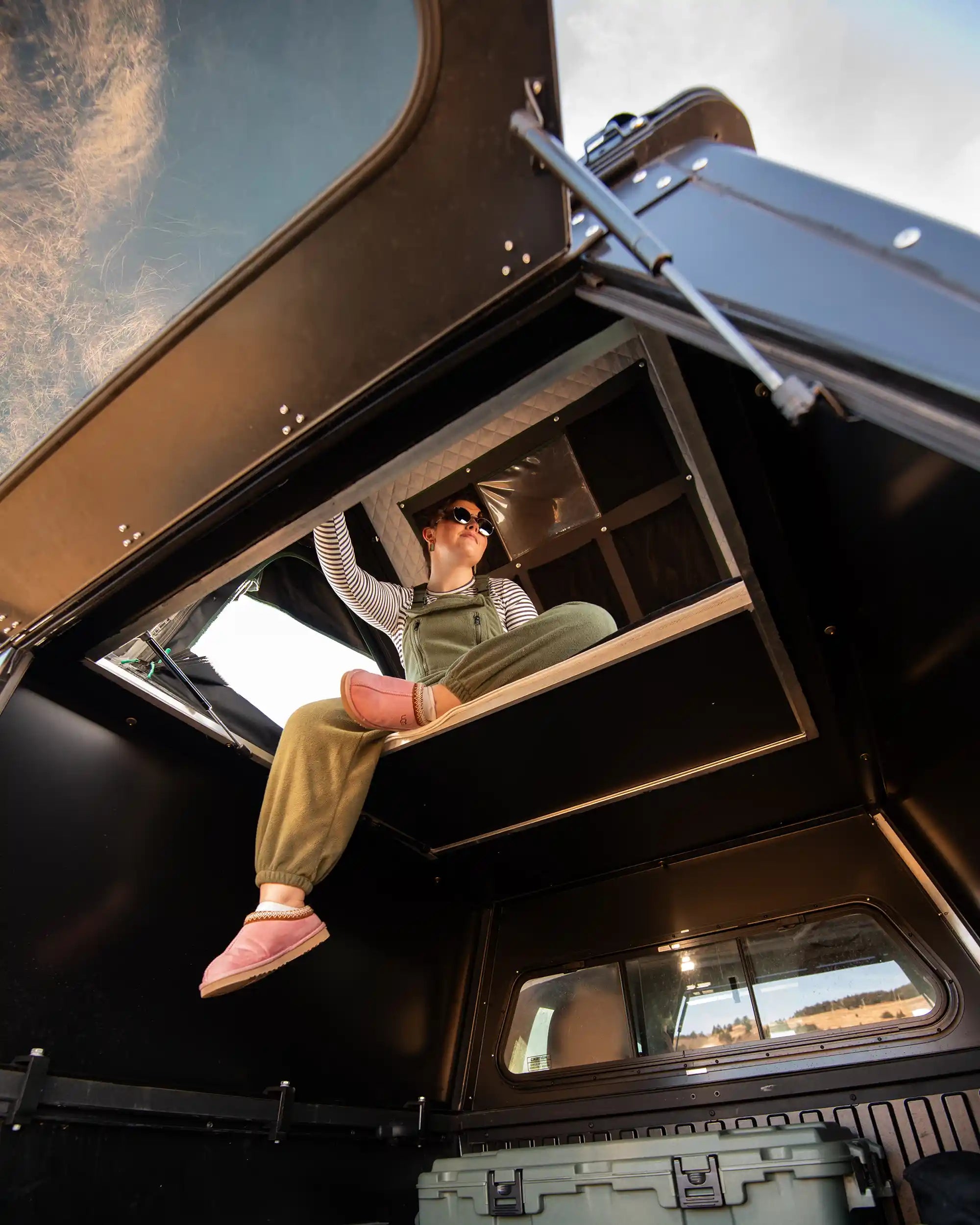 Person sitting inside truck camper with roof top tent with floor panels open