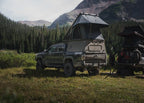 Toyota Tacoma parked in front of mountain with camper shell and rooftop tent.